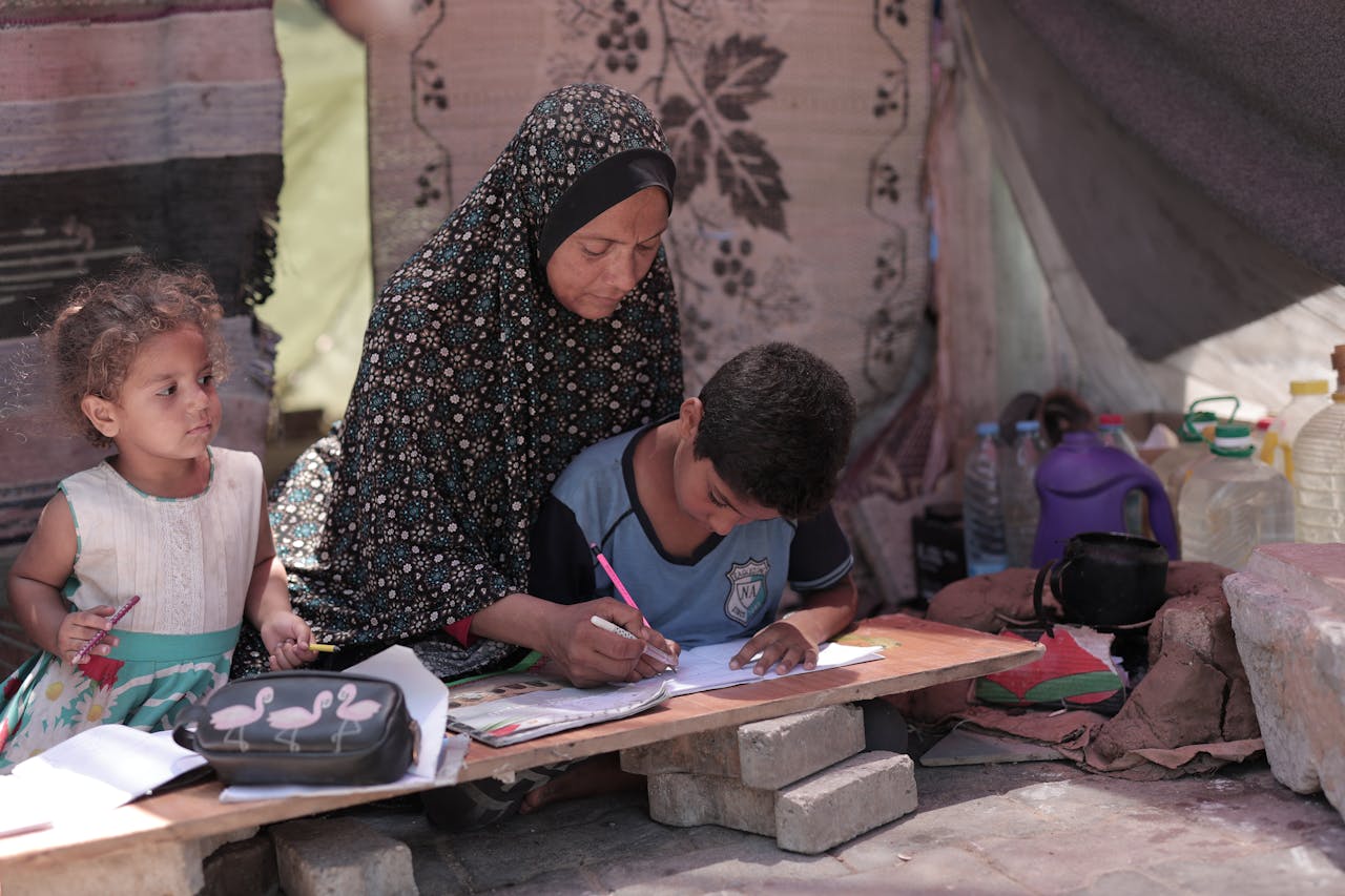 A mother assists her children with their studies in an outdoor setting, fostering education.
